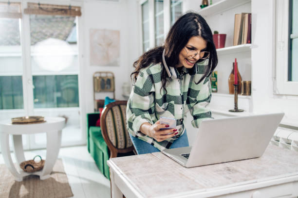 istock Beautiful, young woman using a mobile app and a laptop for banking online 1358223861