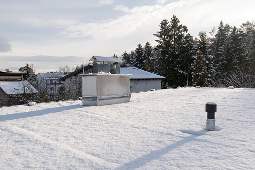 Chimney on a private house on Flat roof covered with snow in the winter season.  Bitumen Asphalt membrane on roof and silver lacquer with