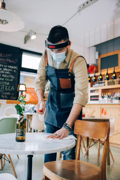 istock Waiter wearing protective face mask disinfecting tables in the restaurant 1358227339