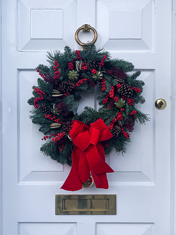 Elegant christmas wreath decorated red berries, pine cones and fir trees on white wooden door