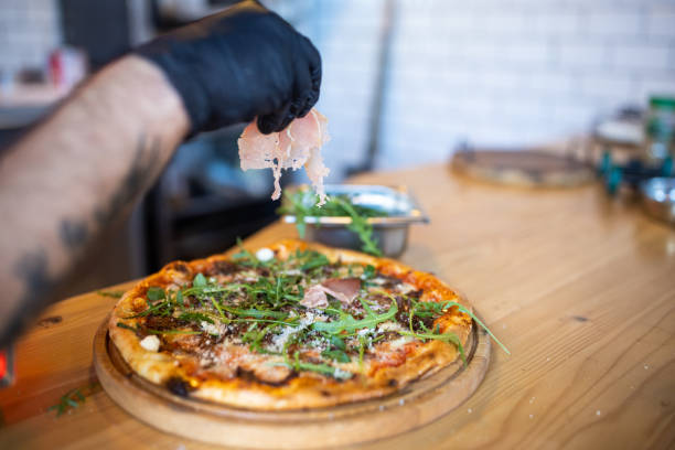 istock Unrecognizable chef adding the slice of prosciutto on pizza 1358229254