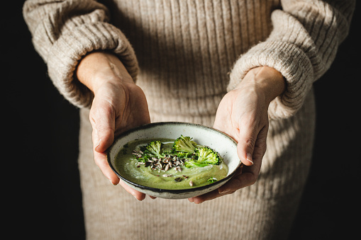 Moody picture of a woman serving tasty broccoli soup