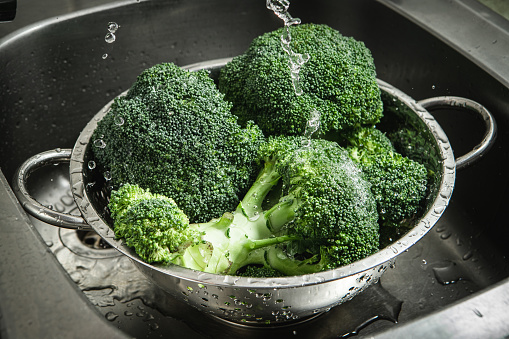 Pouring water onto fresh broccoli to wash it using a sieve