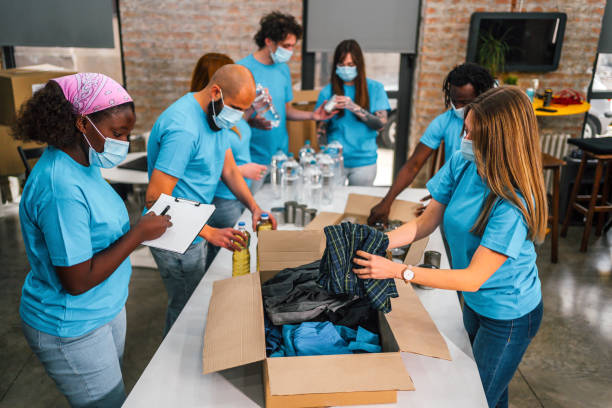 Diverse volunteers team packing donation boxes Young multi racial volunteers sorting, packing food and clothes in cardboard boxes in community charity donations center community center food stock pictures, royalty-free photos & images