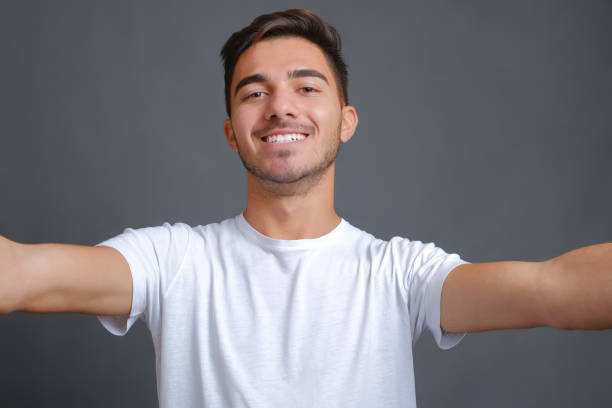 istock Man in a white t-shirt making selfie on a gray background 1358242691