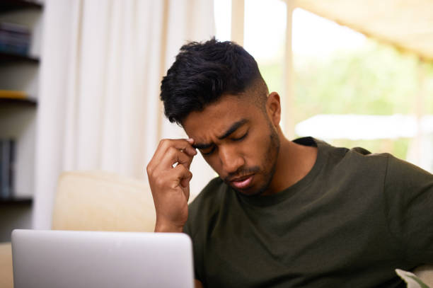 istock Shot of a young man suffering from a headache while using laptop at home 1358246078