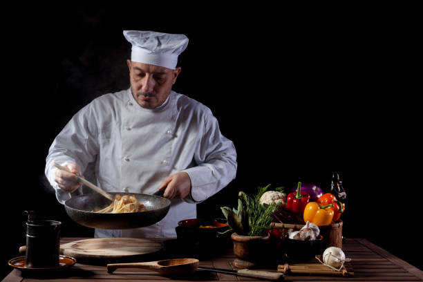 istock Male chef in white uniform preparing spaghetti into cooking pan for cooking pasta with vegetables. 1358248156