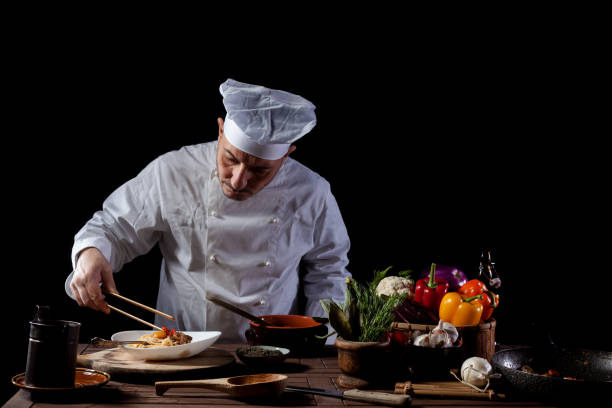 istock Male chef in white uniform prepares spaghetti with vegetables on the dish 1358248161