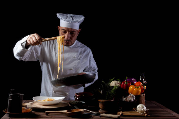 istock Male chef in white uniform prepares spaghetti with vegetables on the dish 1358248176