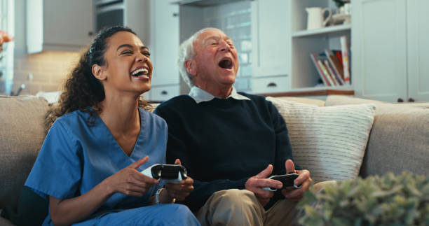 plan d’une jeune infirmière assise et se liant avec sa patiente âgée dans le salon tout en jouant à des jeux vidéo - senior adult leisure games playing care photos et images de collection