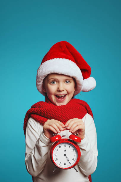 menina usando chapéu de natal e cachecol vermelho segurando despertador, isolado sobre azul - clock clock face blank isolated - fotografias e filmes do acervo