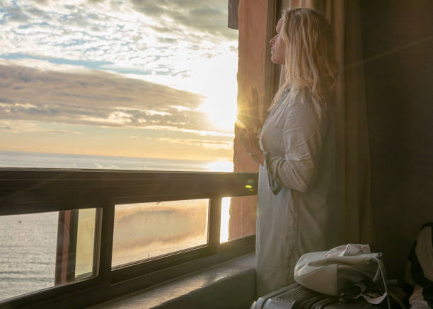 женщина отдыхает у окна, с видом на пляж - looking through window individuality old architecture стоковые фото и изображения