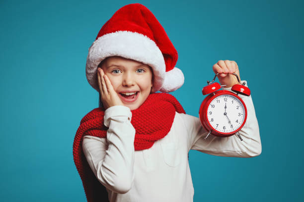 astonished cute girl in santa hat with alarm clock isolated over blue background - clock clock face blank isolated imagens e fotografias de stock