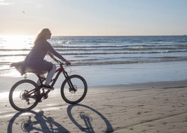 istock Woman bikes down empty beach, at sunrise 1358250897