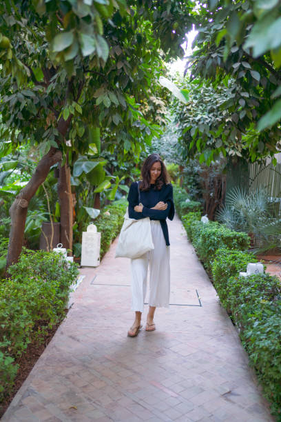 Young woman walks down corridor in lush garden Marrakesh marrakesh riad stock pictures, royalty-free photos & images