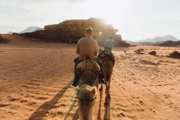 Photo of Friends travelers exploring the Wadi Rum desert riding camels during scenic sunset