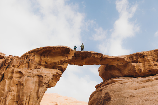 Female and male explorers contemplating the arid landscape walking above the arch in Jordan