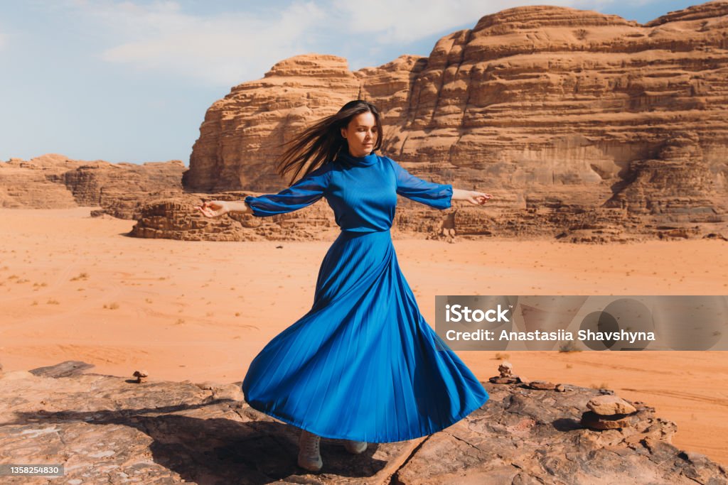 Woman in blue dress contemplating the scenic landscape of Wadi Rum desert Beautiful female in dress walking at the edge of the cliff enjoying the Martian world with red sands and the mountains in Jordan Dress Stock Photo