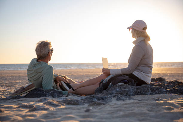 pareja madura se relaja en la playa de arena al amanecer - direct view fotografías e imágenes de stock