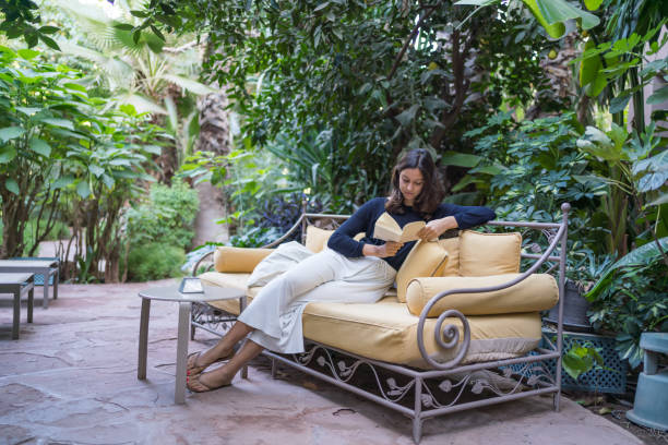 mujer joven se relaja en el sofá con libro en el jardín - outdoors book reading accessibility fotografías e imágenes de stock