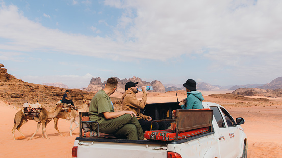 Happy males and females travelers enjoying a road trip by 4x4 vehicle car at the red mountain desert in Jordan
