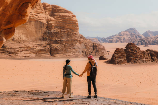Young woman and man traveler contemplating the scenic landscape of Wadi Rum desert Young heterosexual married couple staying at the edge of the cliff looking at the red sands and the mountains of Jordan jordan middle east photos stock pictures, royalty-free photos & images