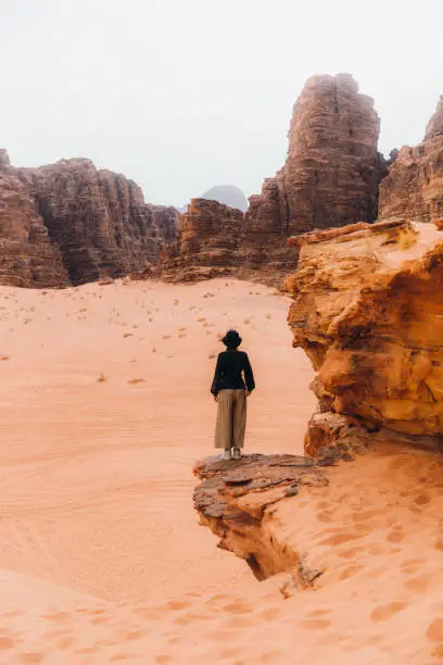Young female explorer staying on the top of the cliff enjoying a view of the picturesque red desert in Jordan