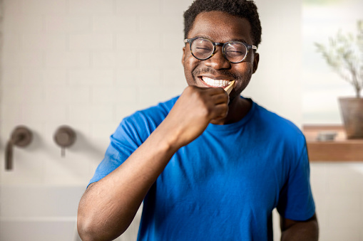 Handsome young black man brushing his teeth in the bathroom at home