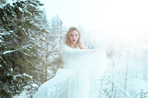 white beautiful young blonde woman in a white dress in winter in the snow in the forest