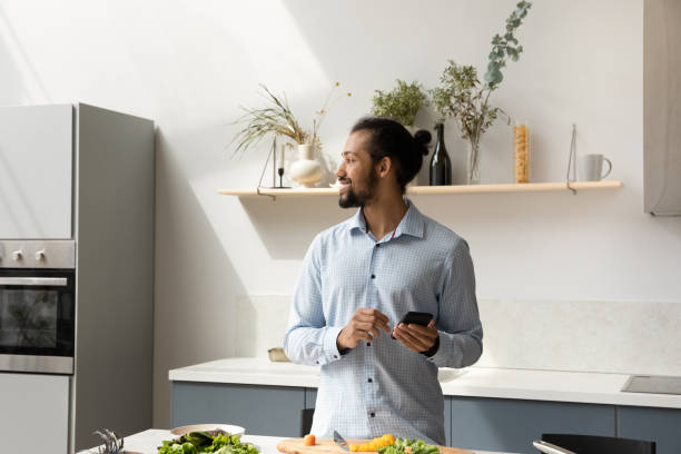 istock Distracted from preparing meal happy African American man using cellphone. 1358265983