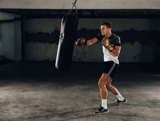 istock Fit professional boxing man kicking at punching bag 1358267074
