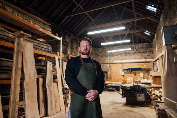 Proud Local Carpenter Carpenter who works with sustainable locally sourced wood in a workshop in the North East of England. He is wearing an apron, standing looking at the camera with his hands crossed in front of him. carpenter portrait stock pictures, royalty-free photos & images