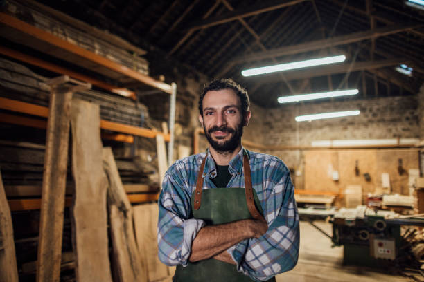 Happy Carpenter Portrait Carpenter who works with sustainable locally sourced wood in a workshop in the North East of England. He is standing looking at the camera with his arms crossed. carpenter portrait stock pictures, royalty-free photos & images