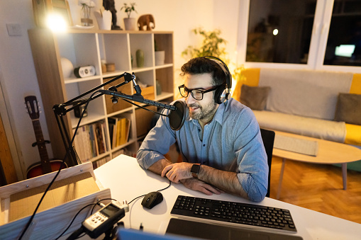 From his modern and cozy home studio, late at night, male Caucasian podcaster and influencer recording his weekly podcast
