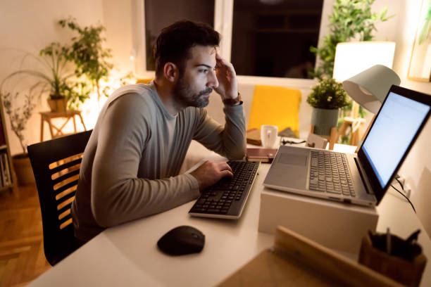 Late at night, stressed man working on laptop from his home office stock photo
