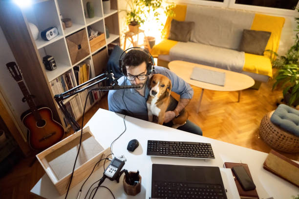 Whiel holding his Beagle dog in the lap, male freelancer talking about some topic on his radio channel Modern Caucasian man, late at night from his home studio recording his podcast while his cute Beagle dog makes him company beagle channel photos stock pictures, royalty-free photos & images
