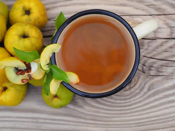 Ripe yellow fruit of the shrub Chaenomeles japonica and a drink in a mug on a wooden background top view. Seasonal autumn quince crop with vitamin C and sour taste and fruit tea. Gardening and cultivation of useful plants