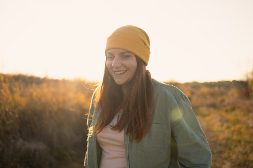 Attractive young woman in bright comfortable casual clothes smiles and enjoys the gentle dawn in the autumn field