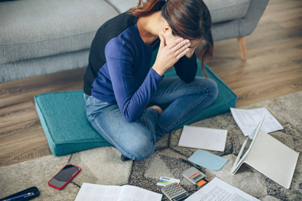 Financial stress Serious concentrated young woman sitting on floor in living room while checking bills at home debt stock pictures, royalty-free photos & images