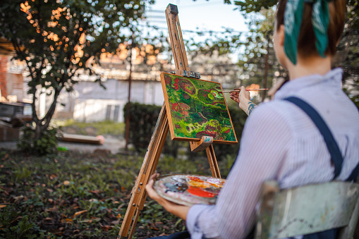 Young beautiful woman painting on canvas with brush outdoors