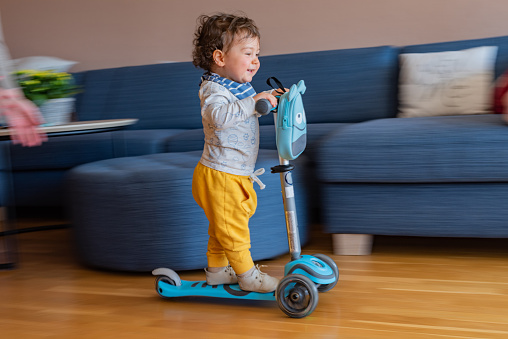 Blurred motion of a boy riding scooter in living room