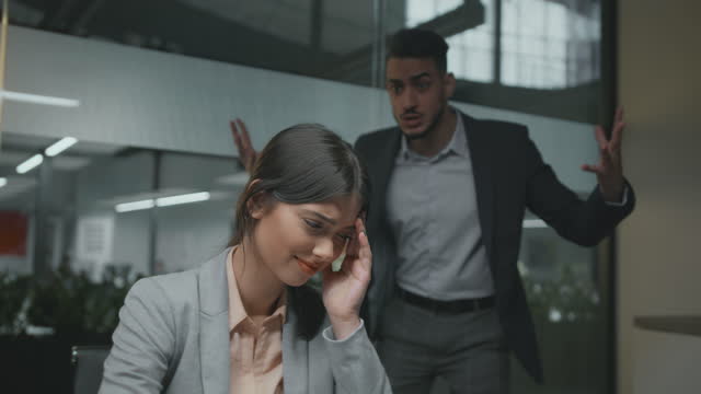Gender discrimination at office. Portrait of young desperate woman employee crying, her angry colleague shouting at her