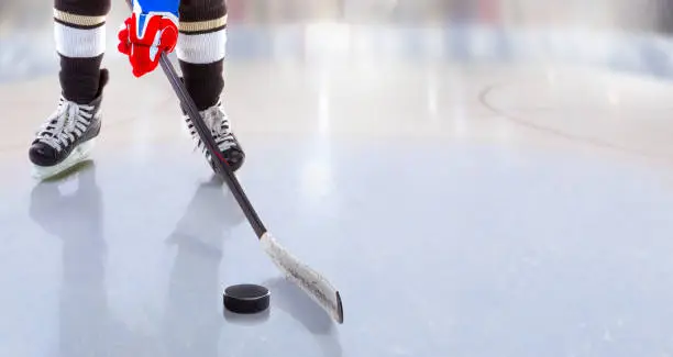 Low angle view of ice hockey player with stick on ice rink controlling puck and copy space.