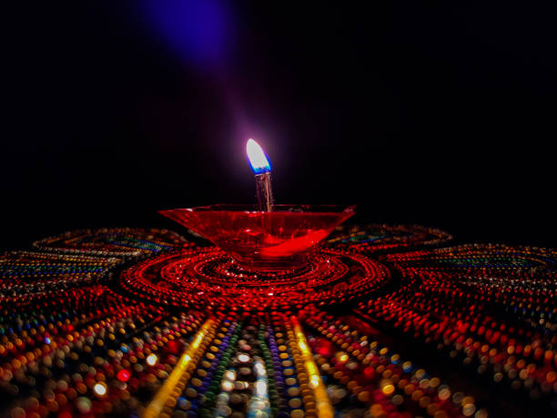 Stock photo of beautiful red color plastic oil lamp lit especially during diwali festival kept on colorful rangoli under dark background. Picture captured at Banglore, Karnataka, India. focus on lamp foto de archivo de la hermosa lámpara de aceite de plástico de color rojo encendida especialmente durante el festival diwali mantenida en colorido rangoli bajo fondo oscuro. imagen capturada en banglore, karnataka, india. enfoque en la lámpara