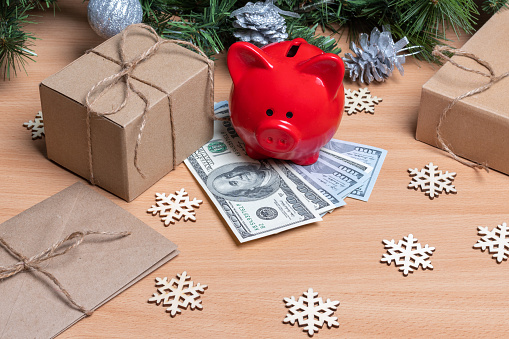 A piggy bank standing on cash dollars on a table with gift boxes, snowflakes and Christmas fir branches. The concept of success and wealth in the new year. New year saving concept