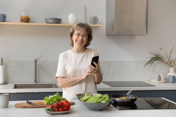 istock Happy mature homeowner woman using mobile phone in kitchen 1358295086