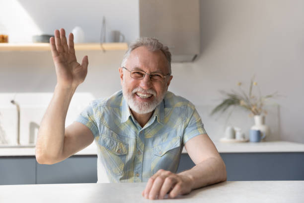 istock Cheerful mature 60s man in glasses waving hello at camera 1358295111