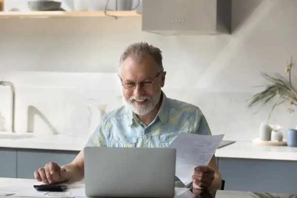 Photo of Happy elder 60s homeowner man getting good news about income