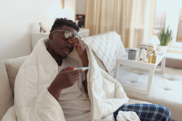 istock Ill man covered with blanket holding thermometer. 1358295570