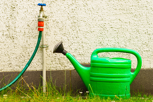 Gardening tools watering green can and tap with hose on garden plot.